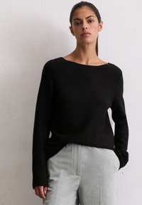 Pulover tricotat negru cu decolteu larg și mâneci lungi; asortat cu pantaloni eleganți gri deschis. Ambele au o textură fină.