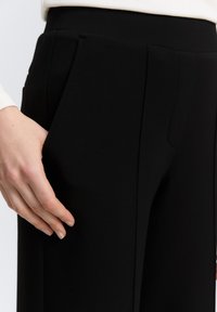 Černé kalhoty na míru z hladkého materiálu, s předními záhyby a bočními kapsami, s dobře padnoucím pasem pro štíhlou siluetu.