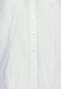 Witte blouse met een soepele textuur, een klassieke kraag en heldere kunststof knopen aan de voorkant.