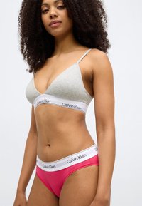 Súprava spodnej bielizne Calvin Klein zahŕňa svetlosivú trojuholníkovú podprsenku a ružové nohavičky v bikínovom štýle s bielym pásikom a logom.