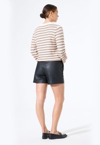 Suéter de crema a rayas con punto texturizado, combinado con pantalones cortos de cuero negros. La vista posterior muestra una silueta ajustada y un diseño elegante. Mocasines negros acentúan el atuendo.