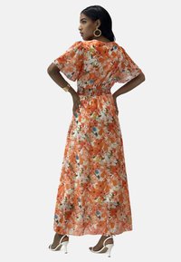 Abito lungo floreale caratterizzato da fiori arancioni e multicolori, tessuto leggero, vita elasticizzata, maniche corte e una silhouette fluida.