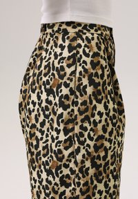 Luipaardprint rok in beige, zwart en bruin. Zachte stof met plooien aan de zijkant, die een gebogen silhouet toont.