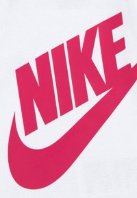 Λευκό μπλουζάκι με μεγάλο ροζ λογότυπο "NIKE" και μια καμπύλη swoosh που εκτείνεται κάτω από το κείμενο. Μαλακή βαμβακερή υφή.