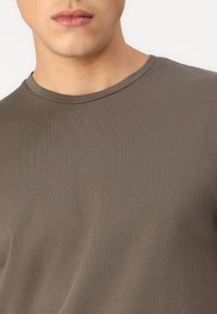 Baumwoll-T-Shirt in dunkelolivgrün, mit rundem Halsausschnitt und kurzen Ärmeln, glatte Textur mit einem subtilen gerippten Muster.
