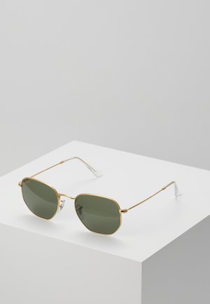 Ochelari de soare din metal aurit cu lentile verzi, formă hexagonală, ramă subțire, vârfuri transparente și logo-ul brandului pe lentilă.