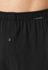 Boxers en coton noir avec une taille élastique, présentant un braguette à un bouton et une petite étiquette tissée sur la taille.