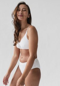 Witte bralette met dunne bandjes en een V-hals, gecombineerd met hooggerande witte slipjes, beide gemaakt van gladde stof.
