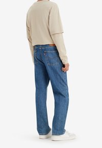 Ljusbeige långärmad skjorta i kombination med blå denimjeans, med rak benklippning, fyra fickor och en läderlogotyp på baksidan.