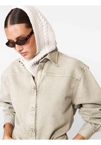 Cămașă din denim bej cu plasă de nasturi, asociată cu o eșarfă tricotată crem texturată și ochelari de soare mici maro.