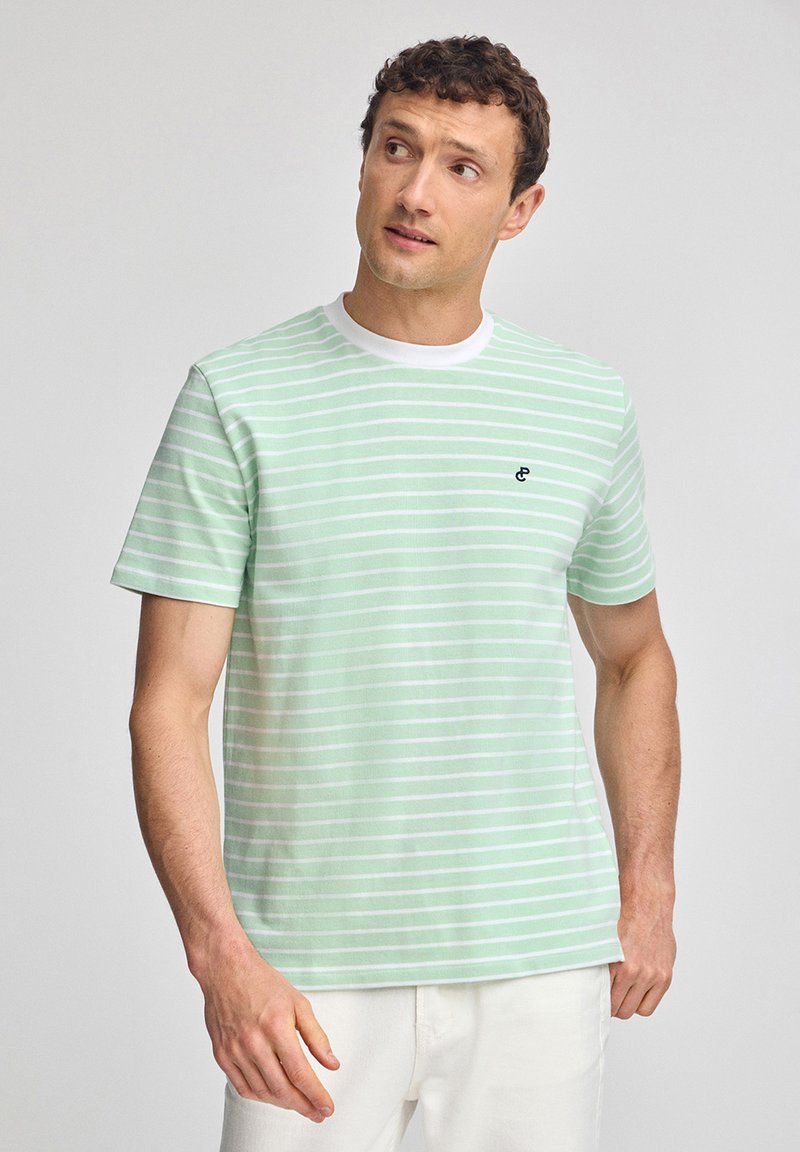 Ljust grön randig t-shirt med vita ränder, med en ribbad vit rund hals och en liten svart logotyp på vänster bröst. Tillverkad av bomull.