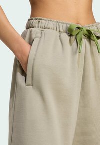 Light beige joggers with an elastic waistband, featuring a green drawstring and side pockets; soft texture and relaxed fit.