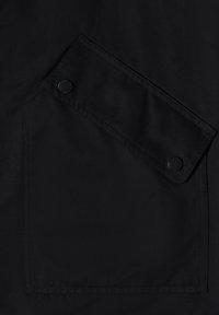 Poche en tissu noir avec un rabat fixé par deux boutons-pression noirs, coutures détaillées autour des bords.