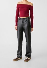 Burgundská top s dlouhým rukávem a off-the-shoulder designem, v přiléhavém střihu, zkombinovaný s černými širokými kalhotami z umělé kůže a hnědými teniskami.