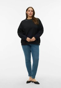 Svart genser med rund hals, pyntet med små nagler langs halslinningen; kombinert med blå, tettsittende jeans og svarte flate sko.