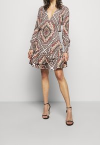 Vestido impreso con mangas largas, escote en V y volantes en capas. Presenta un patrón geométrico en tonos rojos, marrones y crema.