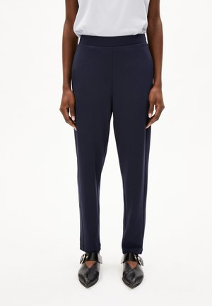 Navy-hohe Hosen aus einem glatten, dehnbaren Stoff mit einer taillierten Passform. Verfügt über ein schlichtes Design und einen dezenten vorderen Bundfalten, kombiniert mit schwarzen Schuhen.