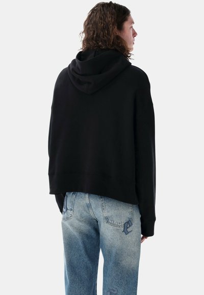 Hoodie corto nero con cappuccio regolabile, in tessuto morbido e vestibilità ampia, abbinato a jeans in denim azzurro chiaro con dettagli ricamati.