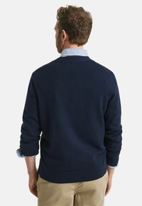 Navyblauer Strickpullover mit Rippbündchen und Saum, über einem hellblauen Hemd mit Kragen getragen. Verfügt über einen klassischen Rundhalsausschnitt und ein strukturiertes Muster.