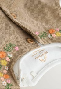Huisje van corduroy in tan met bloemenborduursel in oranje, roze en wit. Voorzien van houten knopen en een witte katoenen halslijn met merklabel.