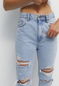 Jeans in denim blu chiaro con effetto usurato, caratterizzati da numerosi strappi e bordi sfrangiati. Design a vita alta con chiusura classica a bottone e zip.