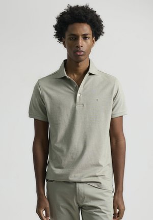 Polo de manga corta y cuello en tejido verde claro. Textura suave con un patrón sutil y un pequeño logo en el pecho.