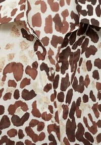 Tissu imprimé animalier brun et crème avec des détails de boutons et de col, ressemblant à des taches de léopard sur une chemise à texture douce.