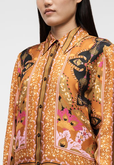 Šilkinė palaidinė šiltos oranžinės spalvos, su sudėtingais rožinių ir juodų gėlių bei abstrakčiais raštais, papuošta juodais mygtukais ir apykakle.