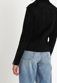 Czarna skórzana kurtka z przylegającym krojem, epauletami na ramionach i bocznymi zamkami. Noszona na jasnoniebieskich, luźnych dżinsach. Miękka faktura.