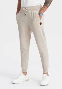 Beige sweatpants gemaakt van zachte stof, met een elastische tailleband met trekkoord, zijzakken en een kleine hexagonale logoaccent.