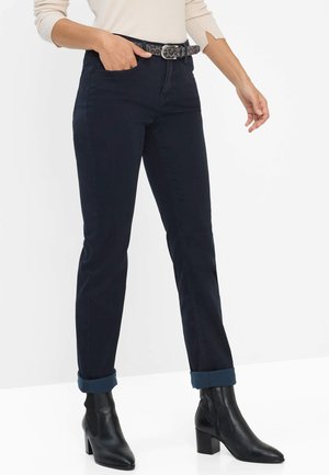 Marineblaue, schmal geschnittene Jeans mit hochgeschlagenen Säumen, kombiniert mit schwarzen, Absatz-Stiefeletten und einem gemusterten Gürtel mit einer silbernen Schnalle.