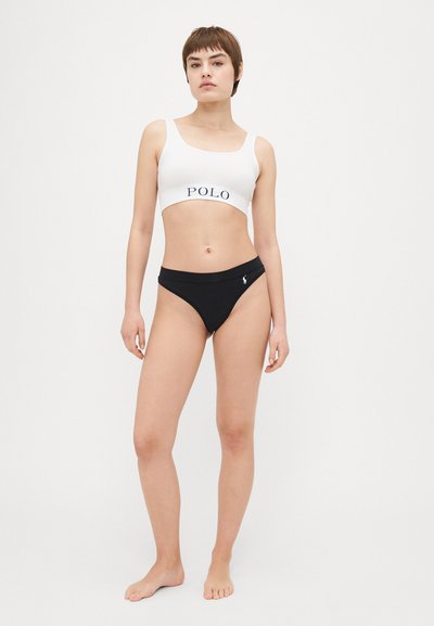 Balts sporta krūšturis ar "POLO" logotipu, apvienots ar melniem bikinī apakšējiem. Abi izgatavoti no gludas, elastīgas auduma. Vienkārša, minimālistiska dizaina.