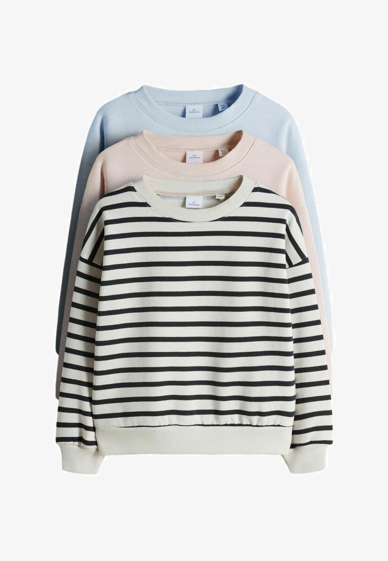 Drie crewneck sweaters opgestapeld, de voorste wit met zwarte horizontale strepen, de middelste lichtroze, de achterste lichtblauw, allemaal met lange mouwen.