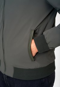 Donkergroen gewatteerde bomberjack met een ritszak, ribgebreide mouwen en zoom, en een gladde, matte buitenkant.