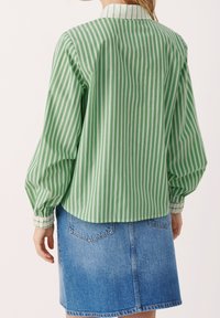 Zeleno-bílý pruhovaný svetr s dlouhými rukávy, nařasenými manžetami a límečkem, doplněný modrou džínovou sukní.