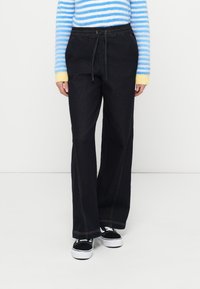 Temno modre jeansa z ohlapnim krojem, elastičnim pasom in vidnimi šivi. Kombinirane z modro-rumeno črtastim puloverjem.