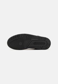 Semelle extérieure en caoutchouc noir d'une basket Jordan avec des motifs de bande de roulement circulaires et linéaires et le mot Jordan embossé près du talon.