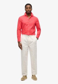 Camisa roja de botones con un bolsillo frontal y cuello, combinada con pantalones de tiro con drawstring de color beige claro y zapatos espadrille en color tostado.