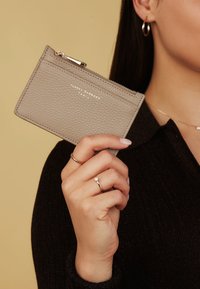 Grijze leren cardholder met textuur en ritssluiting, voorzien van gouden gegraveerde branding en eenvoudige stiksels.