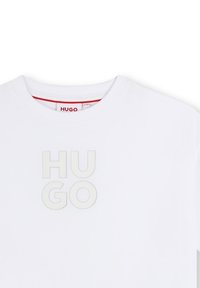 Witte katoenen t-shirt met een ronde hals, voorzien van een verhoogd, lichtgrijs logo "HUGO" op de voorkant, minimalistisch ontwerp, zachte textuur.