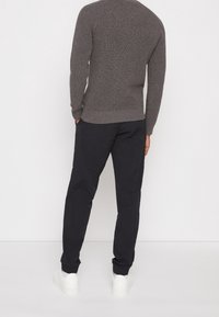 Grauer gestrickter Pullover mit gerippten Bündchen und Saum, kombiniert mit schwarzen schmal geschnittenen Hosen und weißen Turnschuhen. Fokus auf Textur und Farbkontrast.