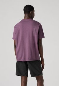 Polo met korte mouwen in paars met een subtiel streepjespatroon, gemaakt van zachte stof. Gdragen met zwarte denim shorts, gezien van achteren.