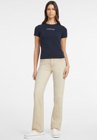 Camiseta marinera de manga corta con el logotipo en blanco "GUESS JEANS", combinada con unos pantalones flare beige claro y zapatillas blancas.