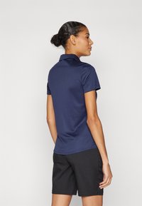 Polo shirt blu navy con colletto, maniche corte e design aderente, abbinato a pantaloni corti neri. Tessuto liscio, dettagli minimi.