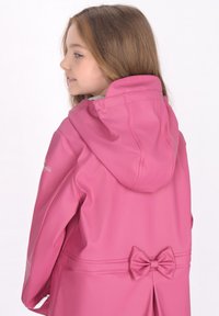 Rosa vattentålig jacka med kapuschong, slät textur och en rosett detalj vid midjan. Designad med praktiska fickor och slitstarkt material.