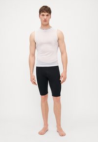 Un haut sans manches blanc avec un motif texturé et un col noir, associé à un short noir ajusté, le tout en tissu extensible.