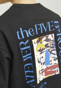 Sudadera negra con un gran diseño gráfico colorido que incluye texto en azul y un patrón abstracto en tonos de amarillo, rojo y marrón.