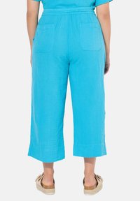Pantalons culottes turquoise en tissu léger et texturé, avec deux poches arrière et une coupe tapered et courte.