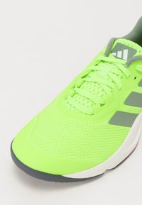 Neon green athletic shoe with a mesh upper, flat laces, grey accents, and a rubber sole. Features a padded collar and branded logo.