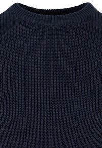 Gros plan sur le tissu en tricot bleu marine d'un pull montrant une texture côtelée épaisse et un col ras du cou.